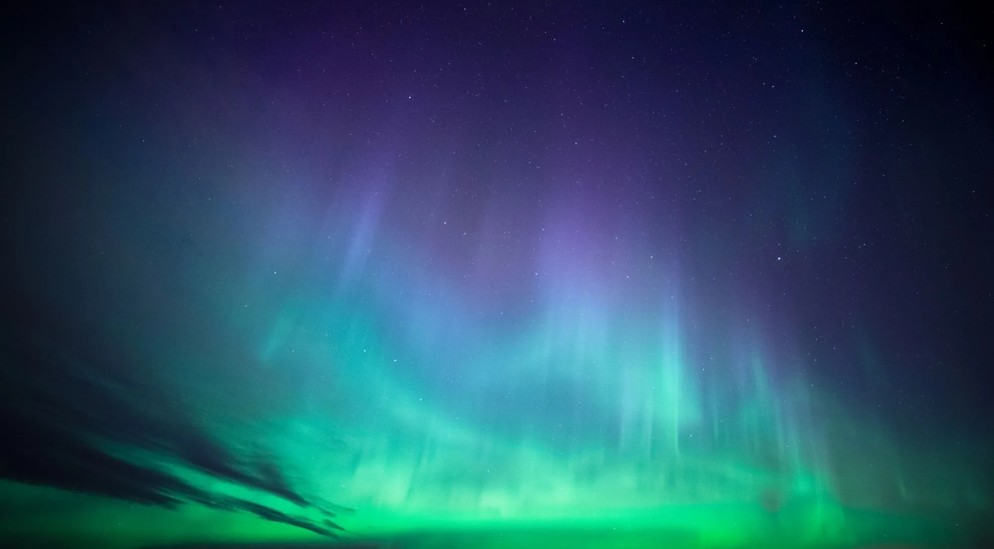 A soft teal-green and violet aurora glow filling the sky above a dark horizon