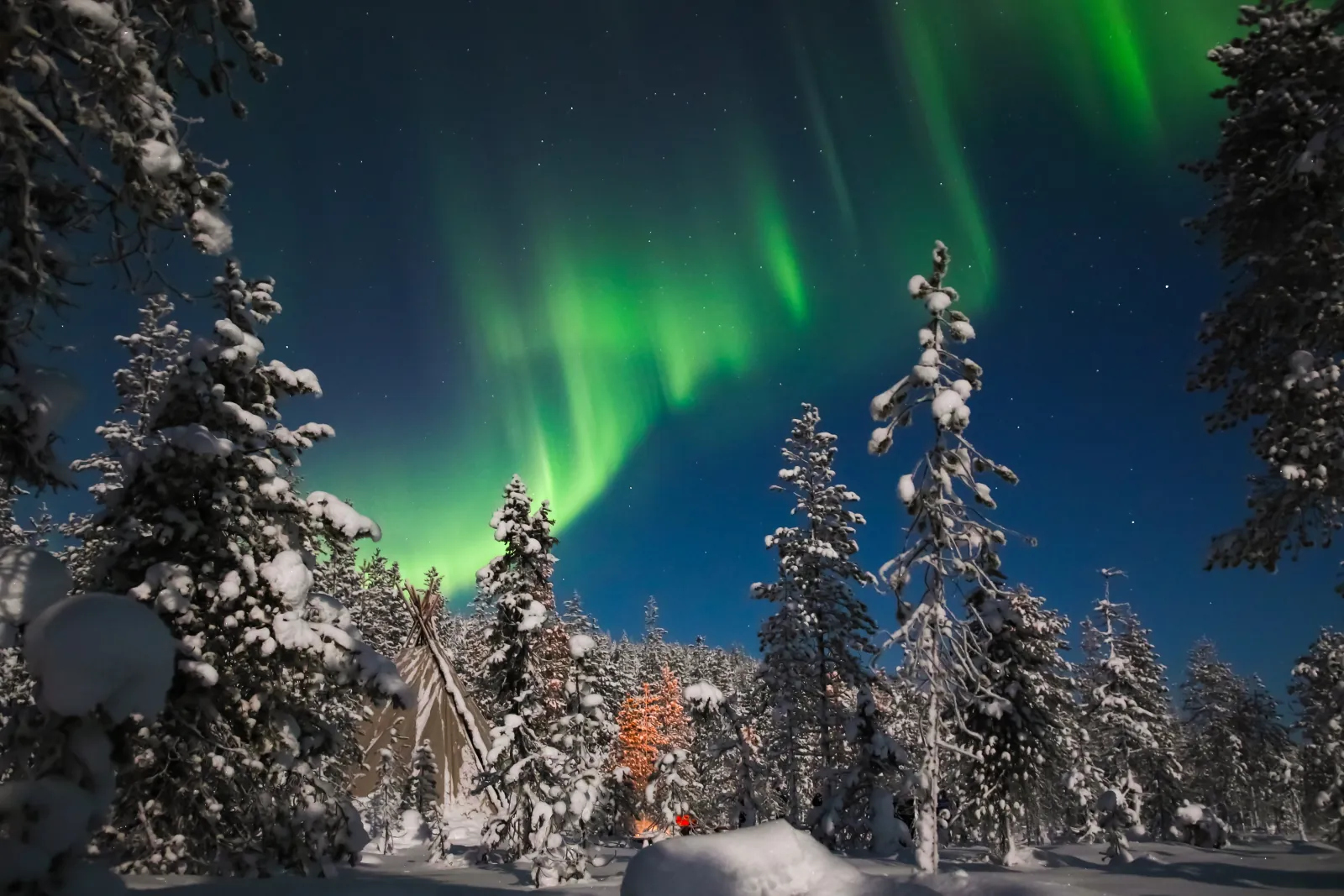 Green aurora over snow-laden pines, a tipi and a glowing campfire in the forest