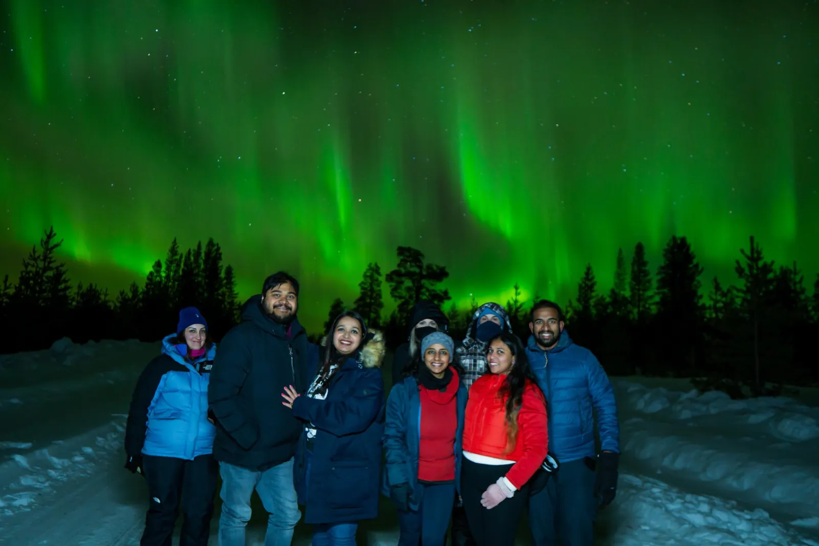 A group of eight guests posing on a snowy road under green aurora curtains