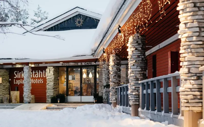 Snow-covered entrance with stone pillars and string lights at Lapland Hotels Sirkantähti in Levi