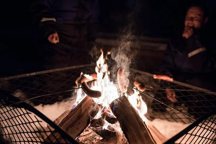 Sausages roasting on sticks over an open fire in a metal fire pit