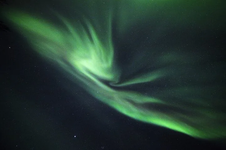 A green aurora corona spiraling across a dark, starry sky
